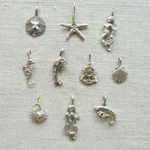 May include: A collection of ten silver-toned metal charms featuring nautical and marine life themes, including a sand dollar, starfish, mermaid, seahorse, dolphin, ship wheel, seashell, nautilus shell, another mermaid, and a shrimp figure.
