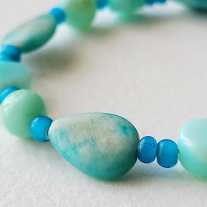 May include: A bracelet made of light blue and turquoise beads. The beads are various shapes and sizes, including oval, round, and teardrop.