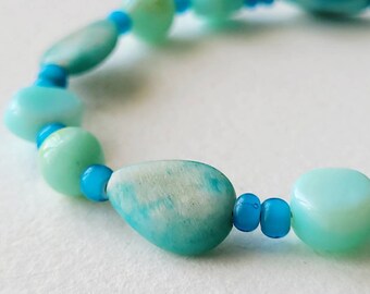May include: A bracelet made of light blue and turquoise beads. The beads are various shapes and sizes, including oval, round, and teardrop.