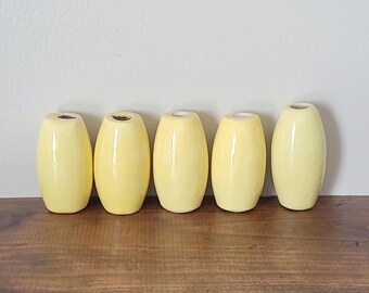 May include: Five yellow ceramic vases, each with a rounded, oval shape. The vases are arranged in a row on a wooden surface.