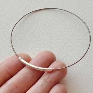 May include: A silver choker necklace with a curved bar clasp.