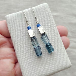 May include: Silver dangle earrings with blue and clear glass beads. The beads are stacked in a graduated size, with the largest bead at the bottom.