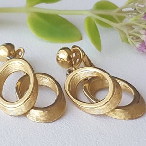 May include: A pair of gold-tone clip-on earrings with a double circle design. The circles are textured and have a brushed finish.