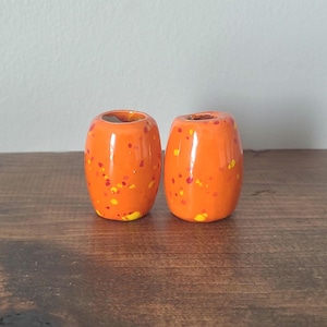 May include: Two orange ceramic beads with yellow and red speckles. The beads are round and have a glossy finish.