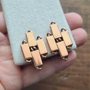 May include: A pair of copper earrings with a geometric design. The earrings are made of interlocking squares and rectangles.