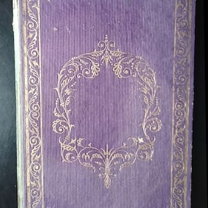 May include: A purple book cover with a gold ornate border and a gold floral design in the center.