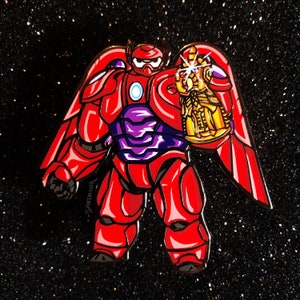 May include: Red and purple enamel pin of a cartoon robot holding a gold Infinity Gauntlet with gems. The robot has a red body, purple chest plate, and a red cape. The pin is set against a black sparkly background.