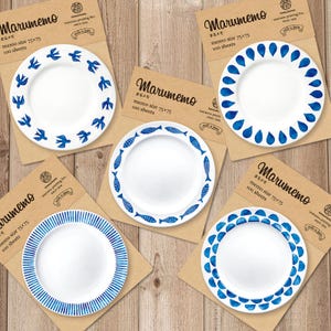 May include: Five white ceramic plates with blue decorative borders, each on a brown paper backing. Designs include birds, teardrops, fish, stripes, and semi-circles. The plates are labelled "Marumemo" with Japanese text and memo size 75x75.
