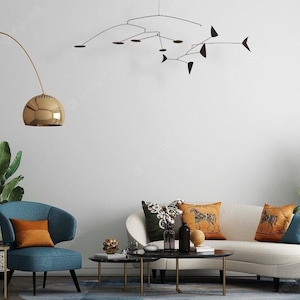 May include: A living room interior with a white couch, a blue armchair, and a coffee table. The couch has a variety of throw pillows, including a brown pillow with a horse design. A gold arc lamp with a round shade hangs over the armchair. A black mobile hangs from the ceiling.