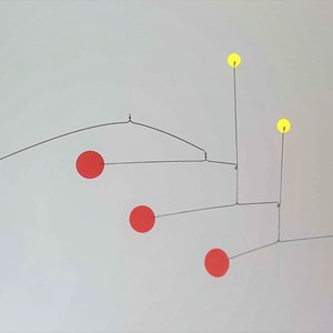 May include: A mobile sculpture with black, red, and yellow spheres suspended from a wire frame. The spheres are connected by thin wires and hang at different levels.