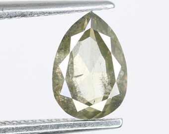 Puede incluir: Una piedra preciosa de diamante verde en forma de pera, sostenida en unas pinzas. El diamante tiene un corte facetado y es de color verde claro.