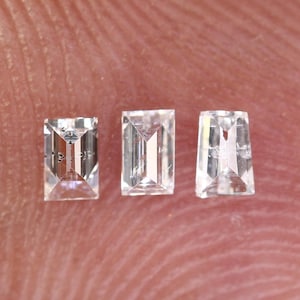 Puede incluir: Tres piedras preciosas rectangulares, facetadas y transparentes sobre un fondo rosa.