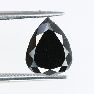 May include: A black pear-shaped diamond held by tweezers against a white background.