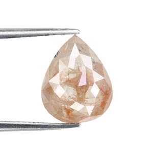 Puede incluir: Un diamante en bruto de forma de pera, de color marrón claro. El diamante está sujeto por unas pinzas.