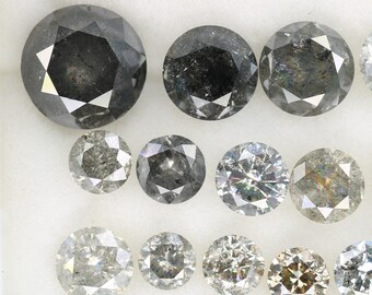 May include: A collection of round, faceted, black and white diamonds. The diamonds are arranged in rows on a white surface.