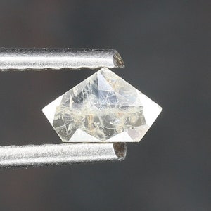 May include: A clear, faceted diamond gemstone held in tweezers. The diamond has a hexagonal shape with a pointed top and a flat bottom.