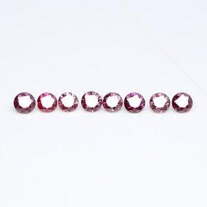 May include: Eight round, faceted gemstones in a row. The gemstones are a deep pink color with a slight purple hue.