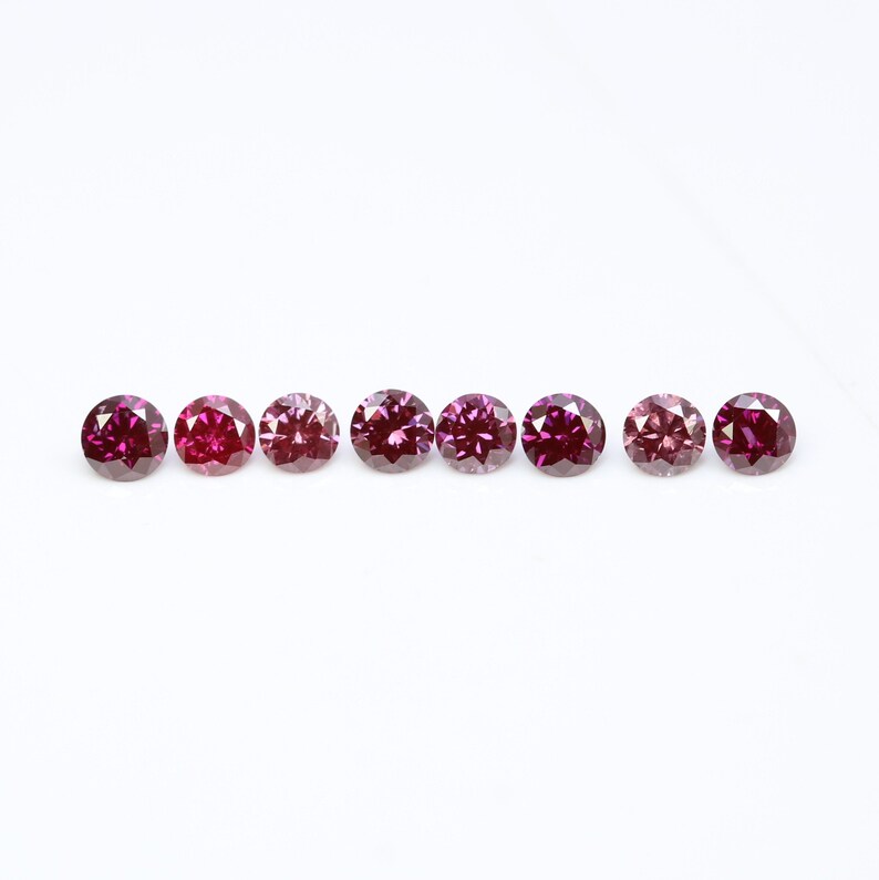 May include: Eight round, faceted gemstones in shades of pink and purple, arranged in a row on a white background.