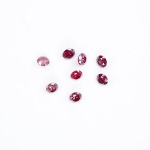 May include: A collection of eight oval-shaped, pink and red gemstones on a white surface.
