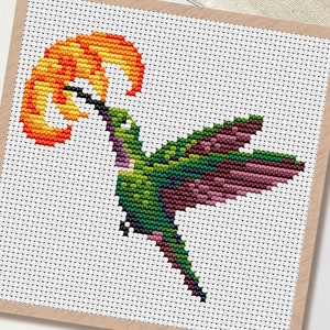 Könnte beinhalten: Kreuzstichmuster eines Kolibris mit grünen, lila und schwarzen Federn, der nach einer gelb-orangenen Blume greift. Das Design befindet sich auf weißem Hintergrund mit Holzrahmen. Das Wort "PDF" befindet sich in einem weißen Kreis.