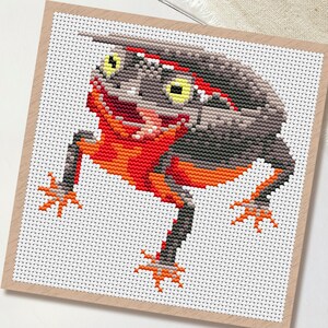 May include: Cross-stitch pattern of a stylized newt in shades of gray, orange, and red. The newt has yellow eyes and is set against a white background. The word "PDF" is in a white circle in the upper left corner. Scissors are in the lower left corner.
