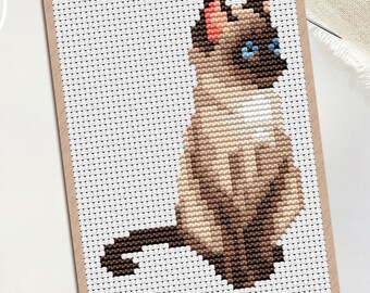 May include: Cross-stitch pattern of a Siamese cat in shades of brown, tan, and black, with blue eyes. The cat is sitting upright on a white background, framed by a tan border. The PDF logo is in the upper left corner.