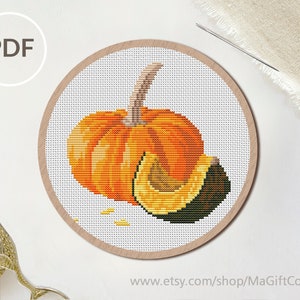 May include: A cross-stitch pattern featuring a vibrant orange pumpkin with a light brown stem and a sliced wedge showing a dark green rind and yellow interior, presented as a PDF file within a circular wooden embroidery hoop frame.