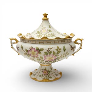 May include: A white porcelain lidded serving dish with a pedestal base. The dish is decorated with pink and yellow floral patterns, green leaves, and gold accents. The handles and rim are trimmed in gold.