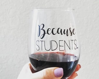 May include: A clear glass wine glass with the text "Because Students." printed on the side. The glass is filled with red wine.