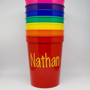 May include: A stack of colorful plastic cups with the name "Nathan" written in yellow on the red cup.