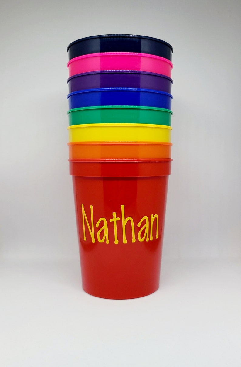 May include: A stack of colorful plastic cups with the name "Nathan" written in yellow on the red cup.
