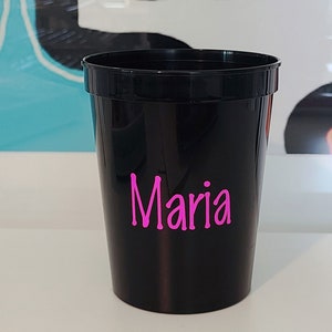 May include: A black plastic cup with the name "Maria" written in pink letters.