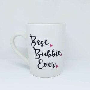 May include: White ceramic mug with black text that reads "Best Bubbie Ever" with pink glitter hearts.