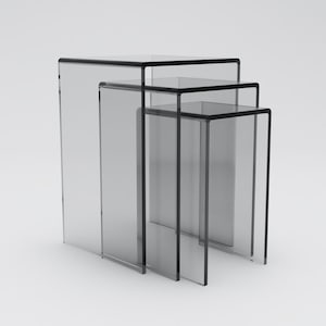 May include: Three clear acrylic nesting tables with black edges. The tables are stacked on top of each other, with the largest table at the bottom and the smallest table at the top.