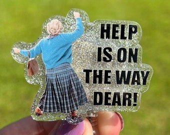 May include: A clear plastic badge holder with a glitter background featuring a photo of a woman with the text "HELP IS ON THE WAY DEAR!"