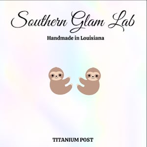 May include: A pair of sloth earrings with a titanium post. The sloths are brown and have a smiling face. The earrings are handmade in Louisiana.