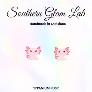 May include: A pair of pink axolotl earrings with titanium posts. The axolotls are cartoon-like and have pink and red details. The earrings are handmade in Louisiana.