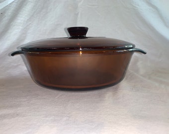 May include: A brown glass casserole dish with a lid. The dish has two handles on the sides and a knob on the lid.