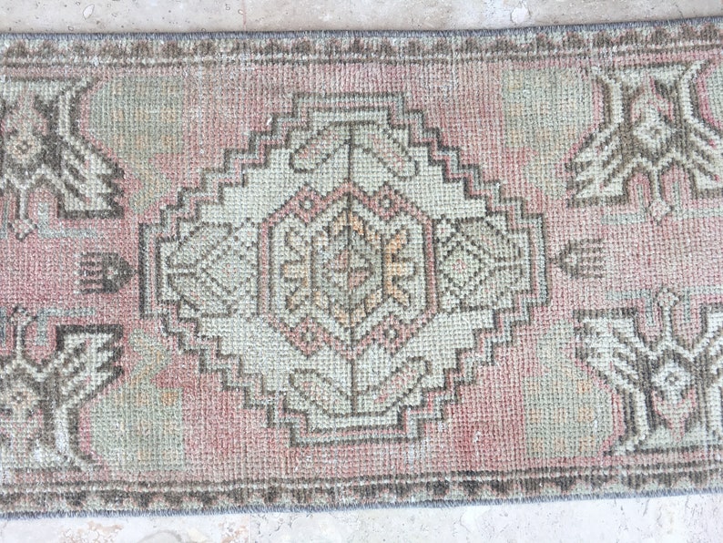 May include: A vintage pink and beige runner rug with a geometric pattern. The rug has a faded look and is made of a woven material.