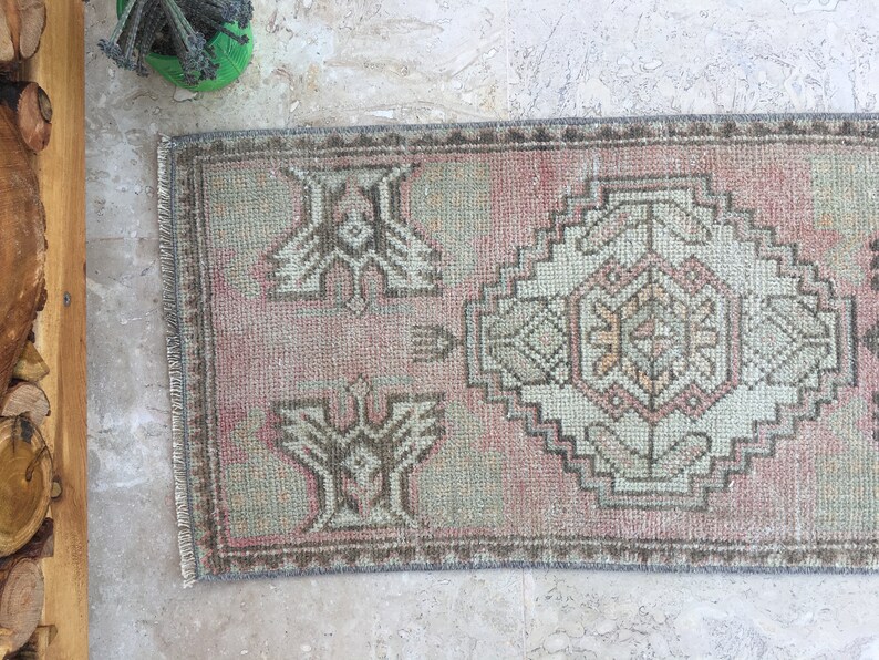 May include: A vintage pink and gray patterned rug with a fringed edge. The rug has a geometric design with a central medallion.