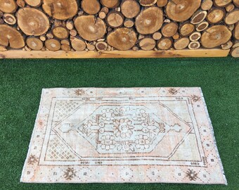 May include: A light pink and brown patterned rug with a geometric design. The rug is on a green artificial grass surface.