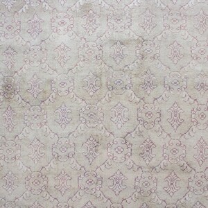 May include: A vintage rug with a cream background and a pink floral pattern. The rug has a pink border.