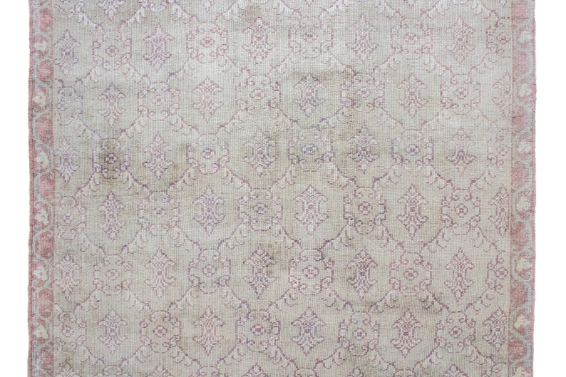May include: A vintage rug with a cream background and a pink floral pattern. The rug has a pink border.