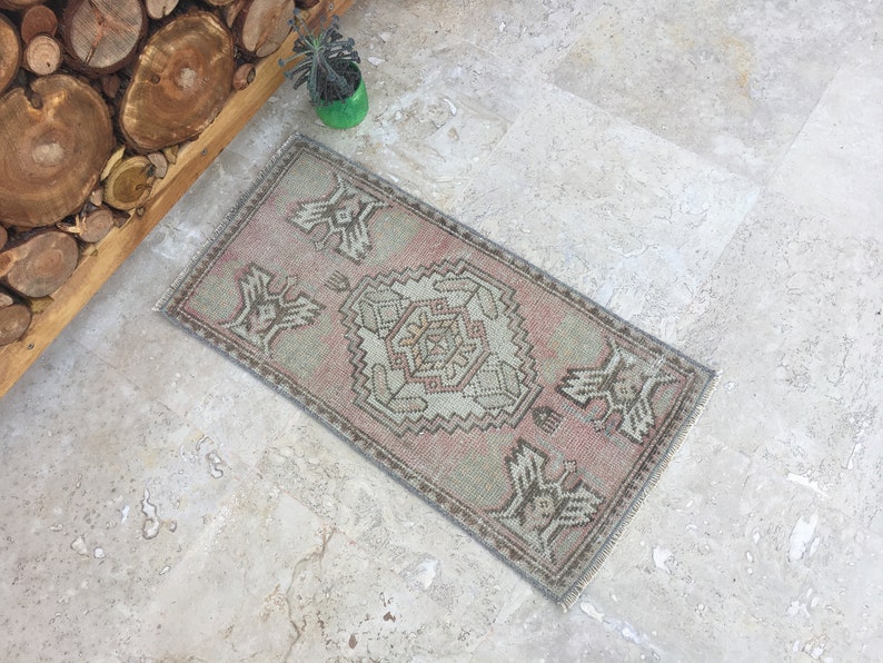 May include: A small, rectangular rug with a traditional Turkish kilim design. The rug is in shades of pink, beige, and gray. It has a geometric pattern with a central diamond shape.