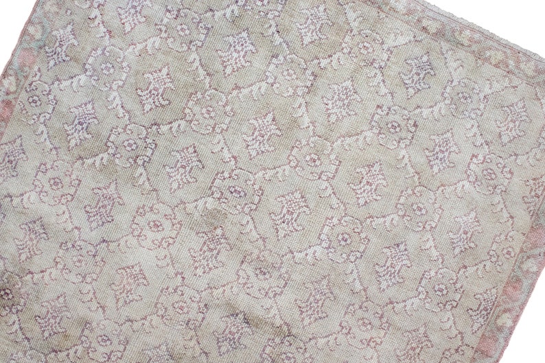 May include: A vintage rug with a cream background and a repeating pattern of pink floral designs.