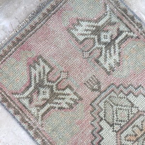 May include: A small, rectangular rug with a pink and gray color scheme. The rug has a traditional design with intricate patterns and a fringed edge.