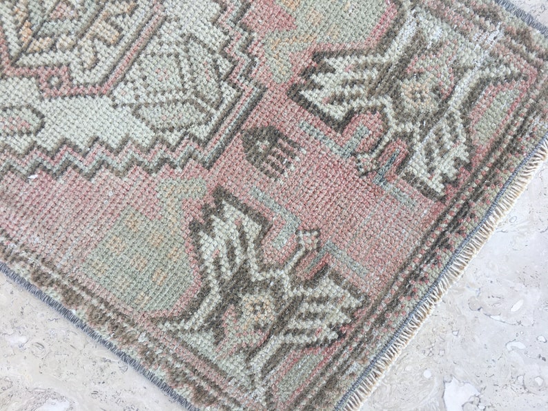 May include: A vintage rug with a faded pink background and a geometric pattern in shades of brown and gray. The rug has a fringed edge.