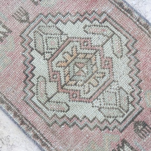 May include: A pink and gray vintage rug with a geometric pattern. The rug has a faded look and is made of wool.
