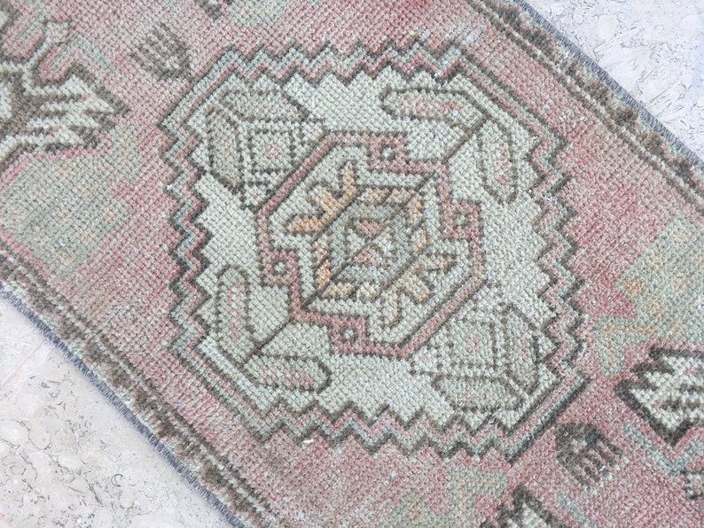 May include: A pink and gray vintage rug with a geometric pattern. The rug has a faded look and is made of wool.