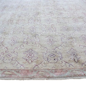 May include: A vintage rug with a cream background and a delicate floral pattern in shades of pink and white. The rug has a fringed edge.